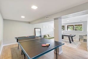 A room with a ping pong table, a pool table, and a green sofa.