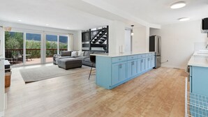 A modern kitchen with blue cabinets, a grey sofa, and a staircase leading to a balcony.