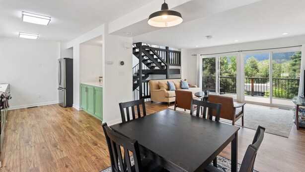 A spacious living area with a dining table, chairs, a staircase, and a large sliding glass door leading to a balcony.