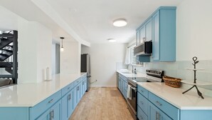 A modern kitchen with blue cabinets, white countertops, and stainless steel appliances.