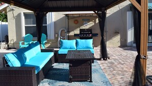An outdoor patio with wicker furniture, a grill, and a covered area.