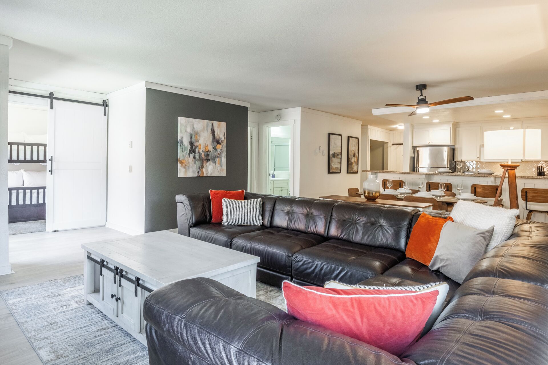 A modern living room with a leather sectional sofa, a white coffee table, and a dining area with wooden chairs and a glass-top table.