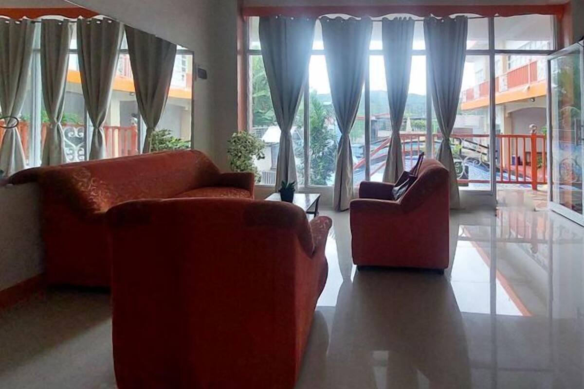 Ein Zimmer mit Sofa und Sesseln, großen Fenstern mit Vorhängen und einem Balkon mit Geländer.