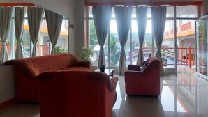 A room with a sofa and armchair, large windows with curtains, and a balcony with a railing. - RedDoorz @ JL Lodging House and Cafe Irosin (Irosin)