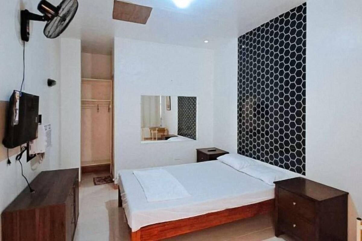 Ein Schlafzimmer mit Bett, Nachttisch, einem an der Wand montierten Fernseher und einem Spiegel.