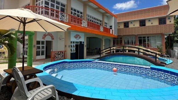 A swimming pool with a tiled deck, a wooden bridge, and a two-story building with a balcony. - RedDoorz @ JL Lodging House and Cafe Irosin (Irosin)