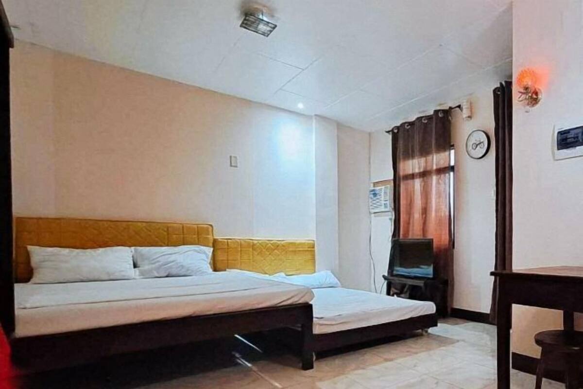 Ein Zimmer mit zwei Betten, einem Fernseher, einer Uhr und einem Fenster mit Vorhängen.