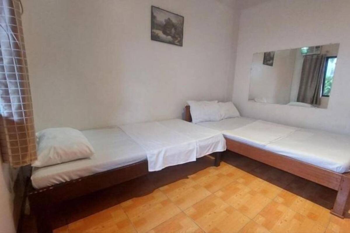 Ein Zimmer mit zwei Einzelbetten, Holzboden, einem Bild an der Wand und einem Spiegel, der einen Teil des Raumes reflektiert.