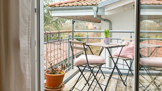 A balcony with a table, chairs, and a potted plant.