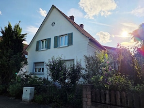 Ein zweigeschossiges Haus mit einem dreieckigen Dach, einem sichtbaren Schornstein und einem kleinen, runden Fenster im Obergeschoss.