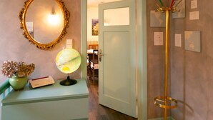 A hallway with a globe, a mirror, a coat rack, and a door leading to another room.