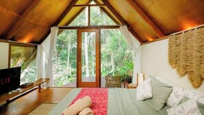 Een slaapkamer met een groot bed, een televisie en uitzicht op het bos.