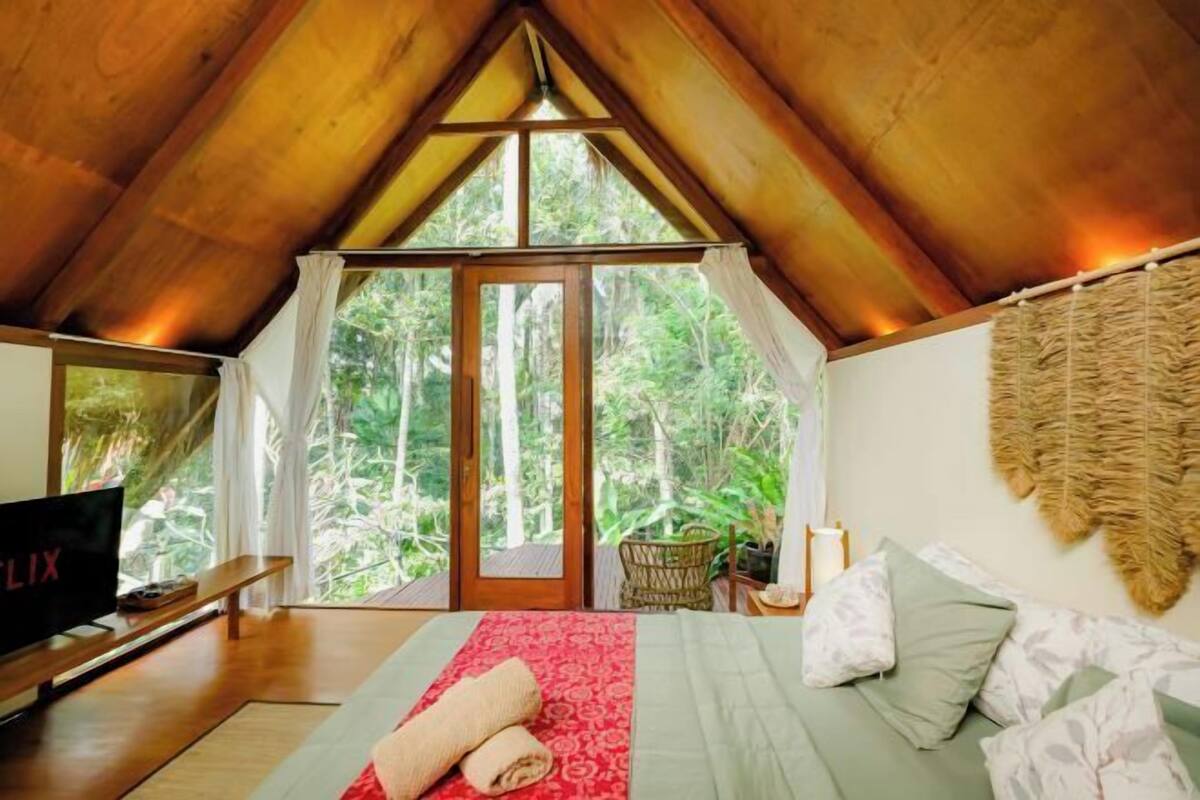 Un dormitorio con una cama grande, televisión y vistas al bosque.