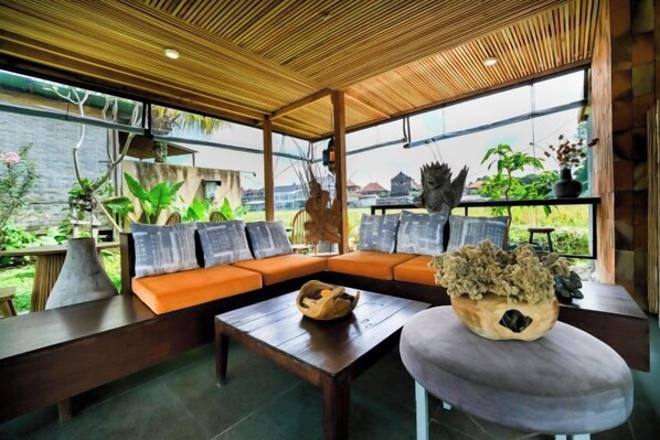 A modern outdoor seating area with a wooden ceiling, a cushioned sofa, a coffee table, and a decorative plant centerpiece. - Ubud Jungle Stay - Mahari by WAHM (Bali)