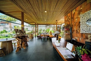 A modern indoor space with a wooden ceiling, a reception desk, seating area, and a view of the outdoors. - Ubud Jungle Stay - Mahari by WAHM (Bali)
