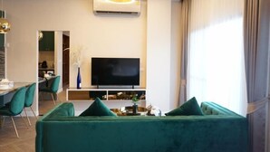 A modern living room with a green sofa, a flat-screen TV, and a dining area with chairs and a table. - The Nine Thasala (Chiang Mai)