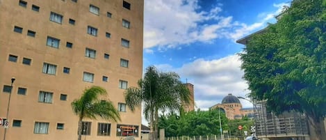 A multi-story hotel with a uniform facade, a central courtyard with palm trees, and a clear sky.