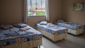 A room with three beds, each with patterned bedding. A window with curtains is visible, and a painting hangs on the wall. - Hotel Santo Afonso (Aparecida)