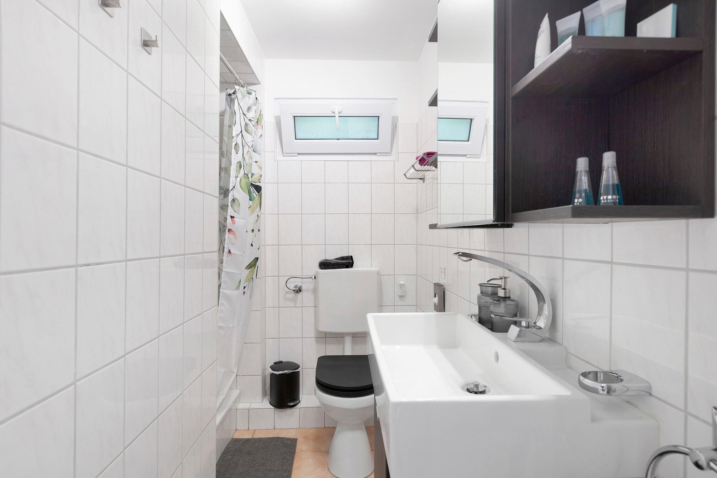A modern bathroom with a toilet, bidet, sink, and a small window.