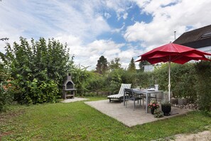 A patio with a grill, a table, chairs, and a red umbrella.