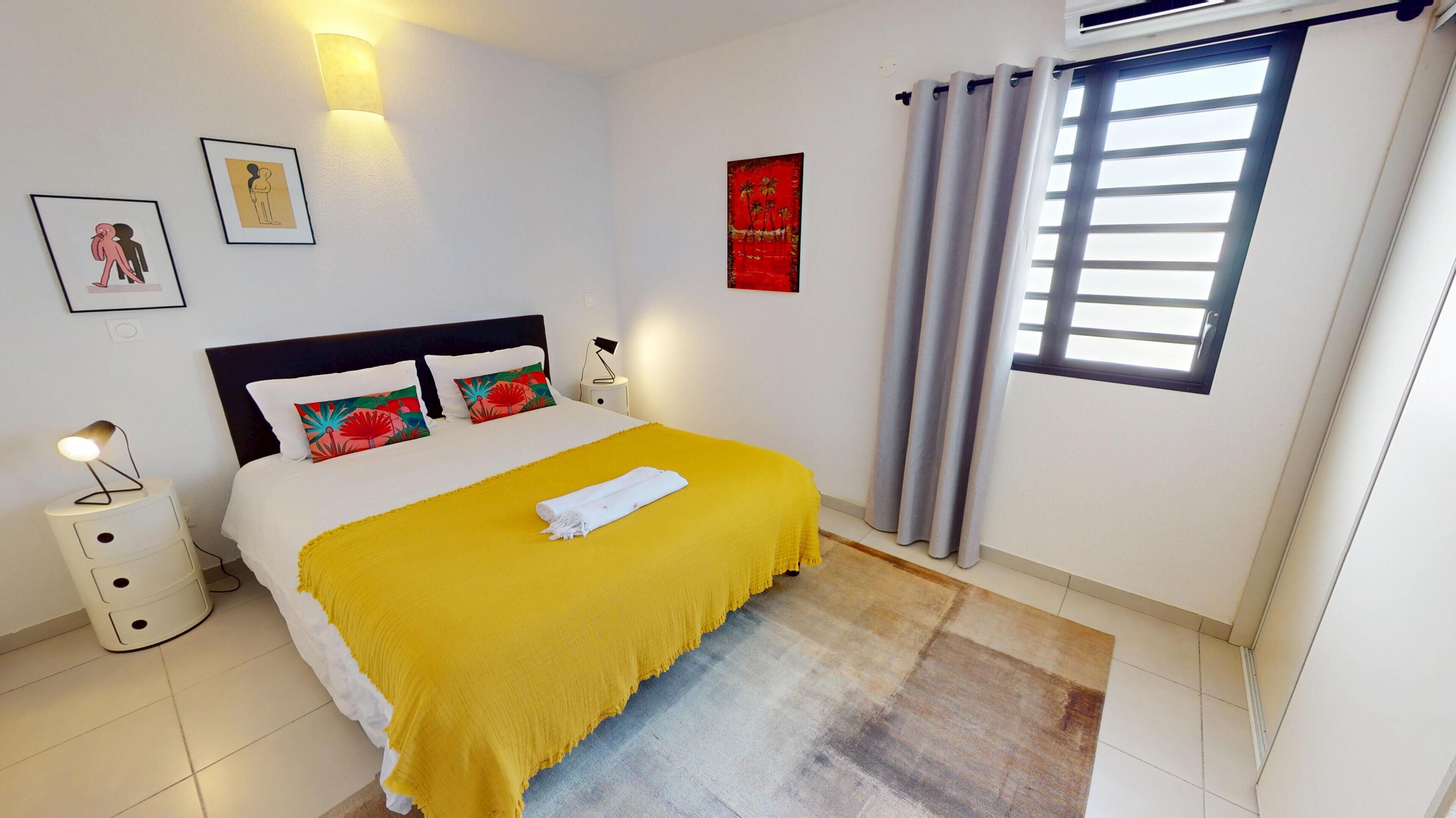 A bedroom with a bed, a nightstand, a lamp, a window with curtains, and wall art.