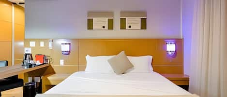 A hotel room with a bed, a desk with a coffee maker, and a wall-mounted TV.