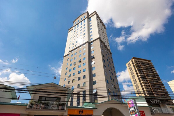 A tall building with multiple floors and numerous windows, surrounded by other buildings and power lines.
