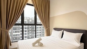 Camera d'albergo con un letto, tende e vista sugli edifici attraverso un'ampia finestra.