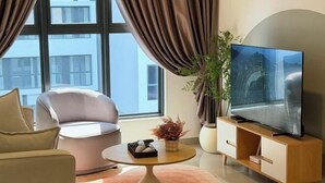 Un soggiorno moderno con un divano, un tavolino da caffè, una TV su un mobile in legno e una grande finestra con tende.