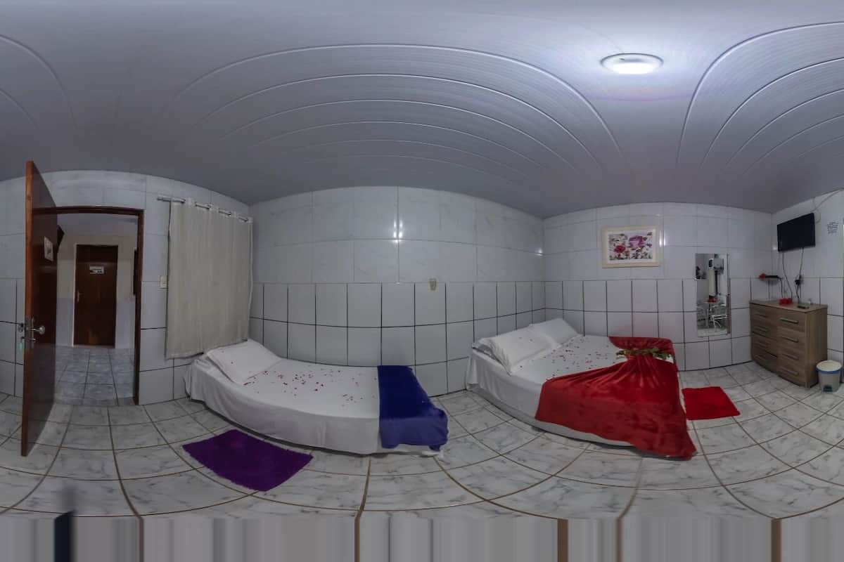 Een kamer met een gebogen bed, een kleine koelkast, een houten kast, een televisie en een badkamer met douchegordijn.