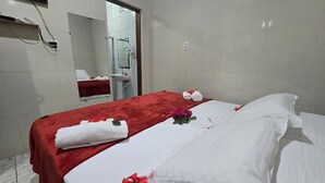 Et hotelværelse med en seng, et rødt håndklæde, hvide sengetøj og en blomsterdekoration.