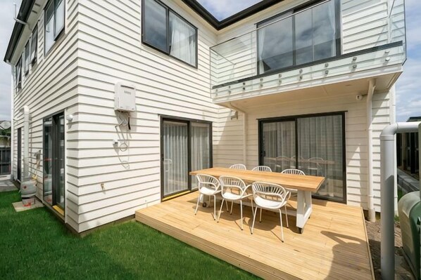 A two-story house with a wooden deck, a dining table with chairs, and a covered patio area. - Auckland Cornwall Park Holiday Homes1 (Auckland)