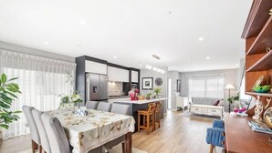 A modern living room with a dining table, kitchen area, and a large window. - Auckland Cornwall Park Holiday Homes1 (Auckland)