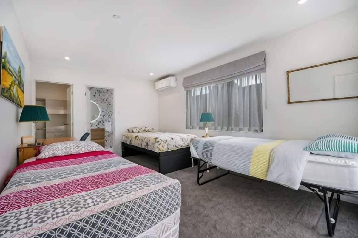 A hotel room with a large bed, a smaller bed, a desk, a chair, a window with curtains, and a painting on the wall.