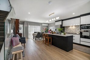 A modern kitchen with a central island, dining area, and a staircase leading to an upper level. - Auckland Cornwall Park Holiday Homes1 (Auckland)