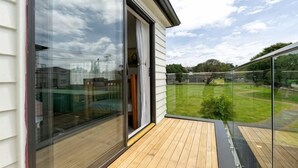 A balcony with a glass door, wooden flooring, and a view of a grassy area. - Auckland Cornwall Park Holiday Homes1 (Auckland)