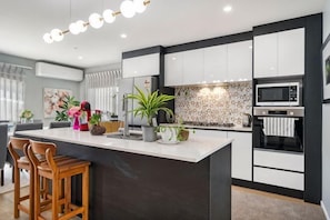 A modern kitchen with a central island, white cabinetry, a microwave, and a coffee machine.