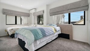 A bedroom with a bed, two windows with curtains, a ceiling fan, and a view of the sky. - Auckland Cornwall Park Holiday Homes1 (Auckland)