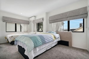 A bedroom with a bed, two windows with curtains, a ceiling fan, and a view of the sky.