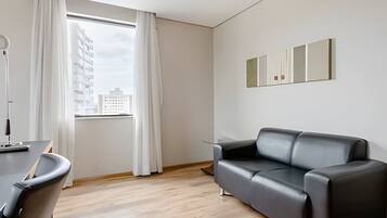 Uma sala de estar moderna com um sofá de couro preto, piso de madeira, uma janela grande com cortinas brancas e uma obra de arte minimalista na parede.