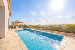 A swimming pool with tiled edges, a stone deck, and a view of buildings in the background. - One-bedroom apartment, with a pool, near Alphaville | 1605 (Osasco)