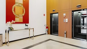 Moderni hissaula, jossa on punainen seinä, pieni pöytä maljakko täynnä kukkia ja palosammutin.