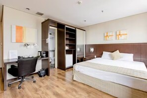 Una habitación de hotel con cama, escritorio, silla, armario y cafetera.