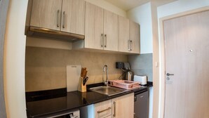 A compact kitchen with light wood cabinets, a black countertop, a sink, and a dish rack. - Silk Valley-Prime located cozy studio (Abu Dhabi)