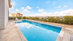 Ein rechteckiger Pool mit Fliesenrand, umgeben von einer Steindeck, mit Blick auf Gebäude im Hintergrund.