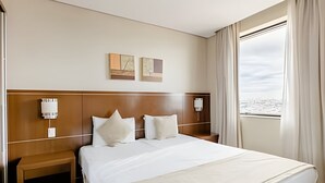 Ein Hotelzimmer mit einem großen Bett, einem Holz-Kopfteil, zwei Wandleuchten, einem Nachttisch und einem Fenster mit Meerblick.