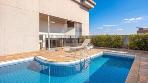 A swimming pool with a tiled deck, a lounge chair, and a small covered seating area. - Apartment with 1 parking space | UN1105 (Osasco)