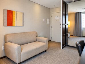 A hotel room with a sofa, a glass table, a door leading to a bathroom, and a view of the room through the door. - 1-bedroom apartment, with a pool, near Alphaville | 1105 (Osasco)