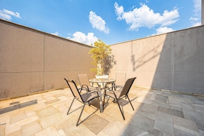 An outdoor patio with a round table and four chairs, a potted plant, and a clear blue sky. - 1-bedroom apartment, with a pool, near Alphaville | 1105 (Osasco)