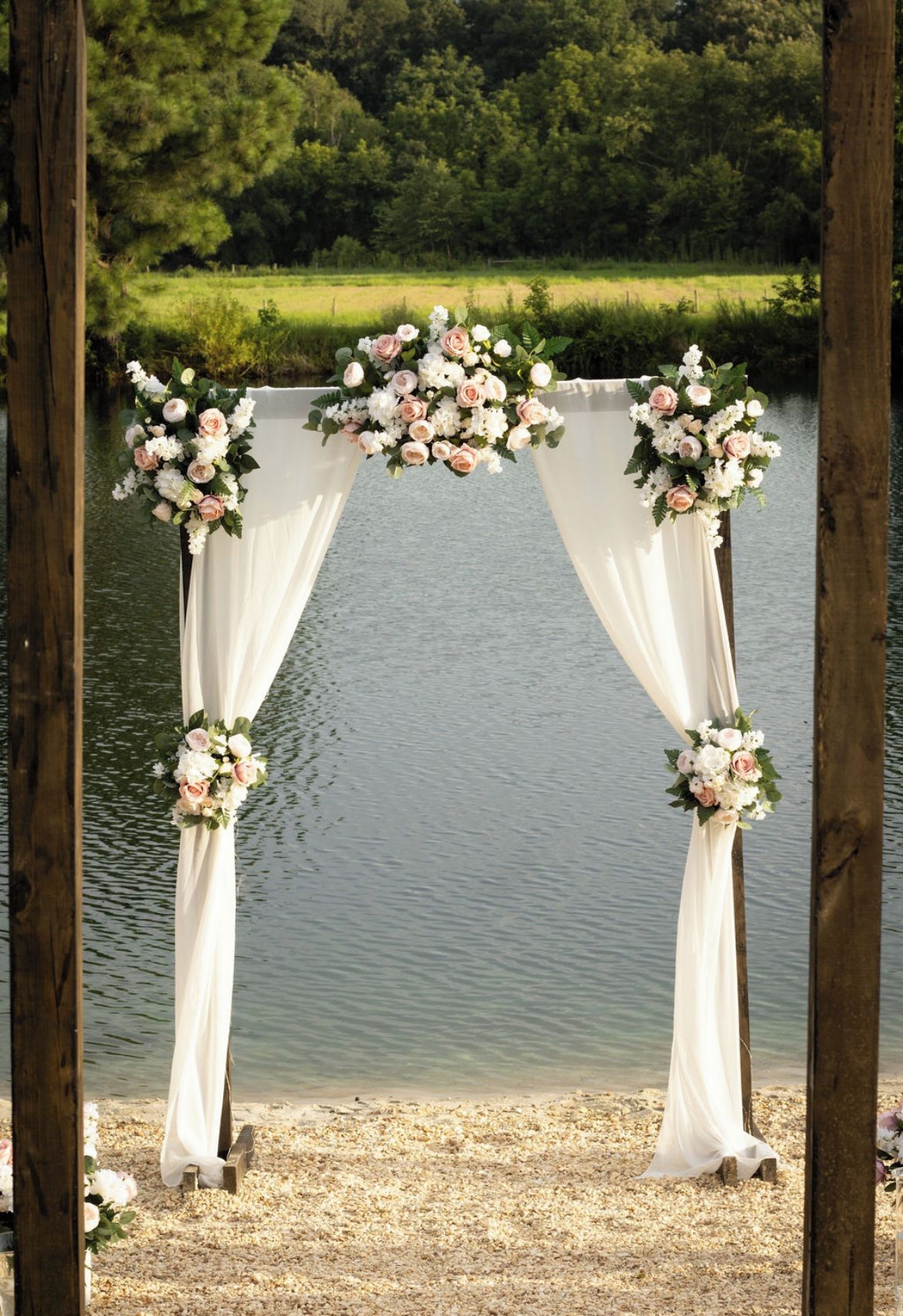 Une arche en bois, agrémentée de draperies blanches et de compositions florales, se dressant sur fond de paysage lacustre.